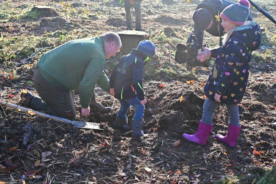 Förster und Kinder setzen einen jungen Baum